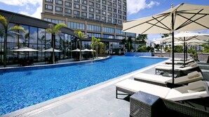A modern hotel pool area with lounge chairs and umbrellas, surrounded by palm trees and a tall building in the background. - Roygent Parks Hai Phong (Hai Phong)