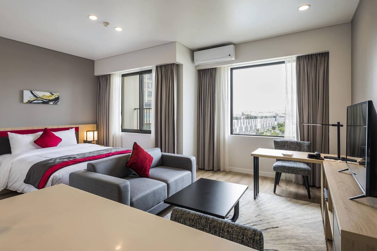 Une chambre d’hôtel équipée d’un lit, d’un canapé, d’un bureau, d’une télévision et de grandes fenêtres.