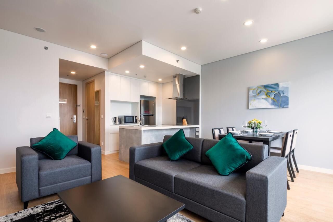 A modern living room with grey sofas and a black coffee table, a dining area with a table set for four, and a kitchen area with a microwave and stove.