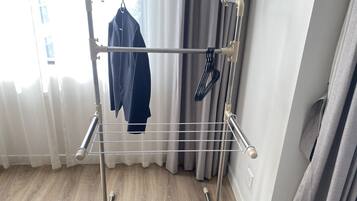 Un tendedero metálico con ropa colgada, ubicado cerca de una ventana con cortinas.