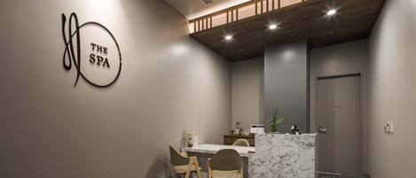 A modern spa room with a marble reception desk, two wooden chairs, and a wall-mounted sign reading "THE SPA".