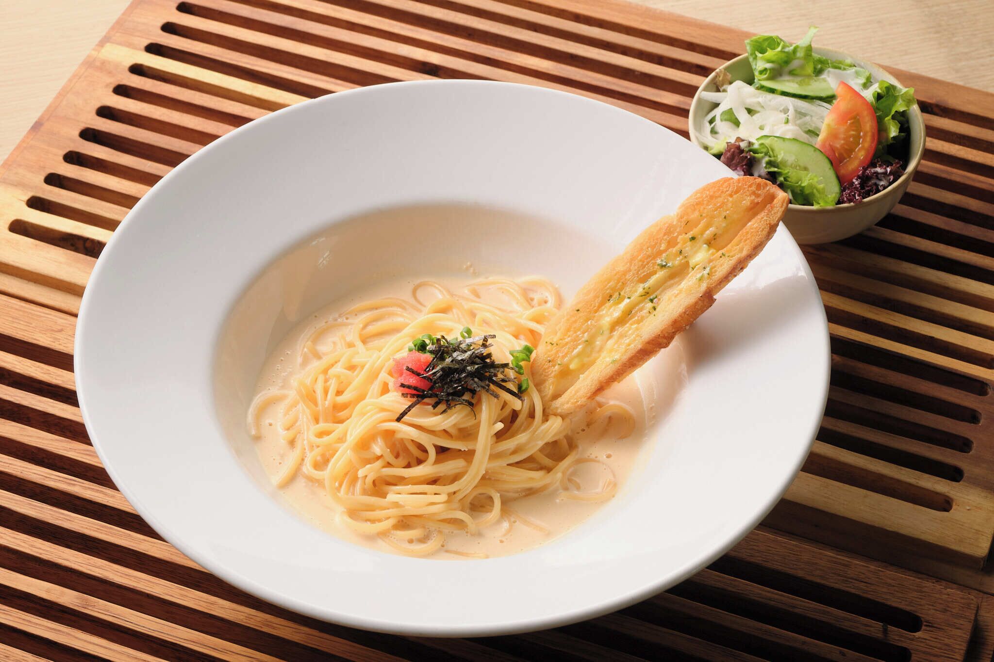 A bowl of pasta with a piece of bread on the side, placed on a wooden table.