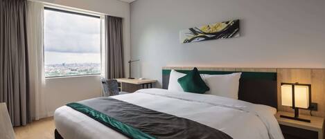 A hotel room with a large bed, a nightstand with a lamp, a window with curtains, and a city view.