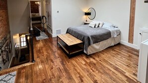 Une chambre avec un puits de lumière, un plancher en bois, un lit, une table de chevet et une lampe fixée au mur.
