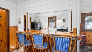 Una cocina con barra de madera, tres sillas azul y blanco a cuadros, un refrigerador y una estufa.