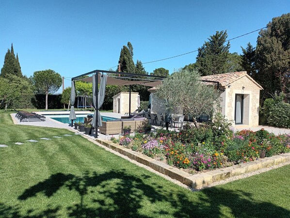 A poolside area with a covered seating area, a stone building, and a flower bed.