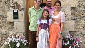 Une famille se tient devant un bâtiment en pierre, dont la porte est en bois. De chaque côté de la porte, on peut voir deux pots de fleurs.