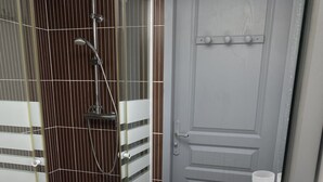Un baño con cabina de ducha de vidrio, un lavabo blanco con espejo y una puerta con perchero para toallas.