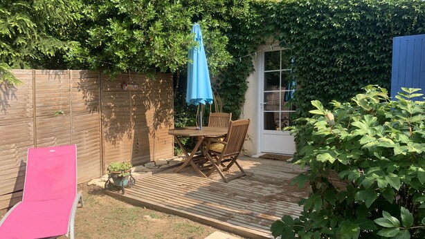 Un patio con una mesa y sillas de madera, una sombrilla azul y una silla reclinable rosa.