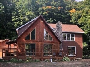 A wooden cabin with a stone chimney, large windows, and a porch.
