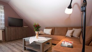 Una sala de estar con un televisor sobre un mueble de madera, una mesa de centro con un jarrón de flores, un sofá con cojines y una lámpara de pie.