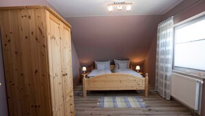 Un dormitorio con cama de madera, dos lámparas de noche, una ventana con cortinas y un radiador.