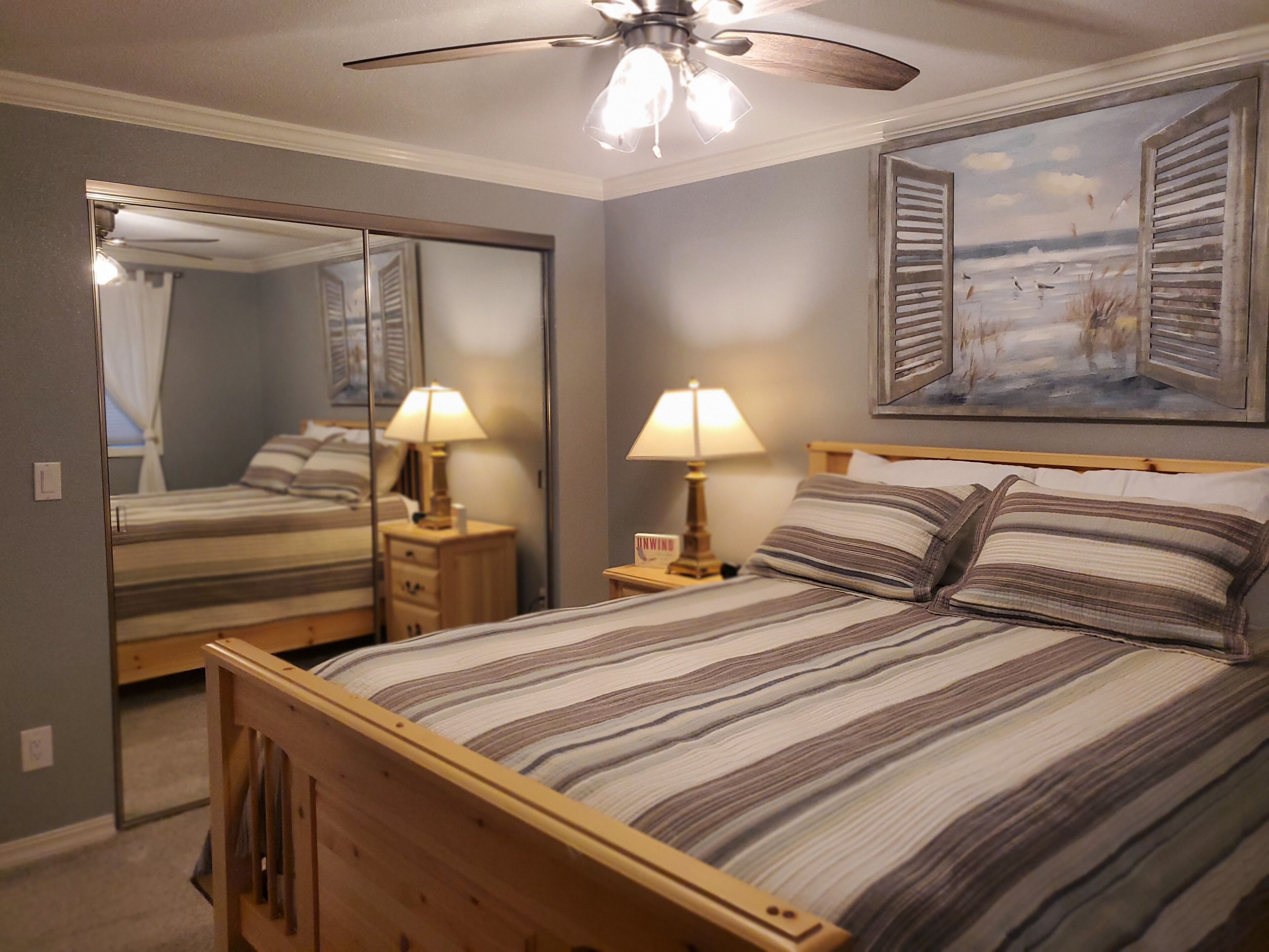A bedroom with a bed, bedside lamps, a ceiling fan, a mirror, and a painting on the wall.
