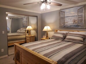 A bedroom with a bed, bedside lamps, a ceiling fan, a mirror, and a painting on the wall. - "By The Sea" Oceanfront Updated Rainbow Rock Condo, Spectacular Views, 1st Floor (Brookings, OR 97415)