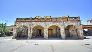 A stone building with three arches and a flat roof with potted plants.