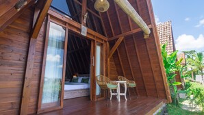 A wooden cabin with a balcony, a bed, wicker chairs, and a small table. - Alam Kawi Ubud Resort & Spa (Ubud)