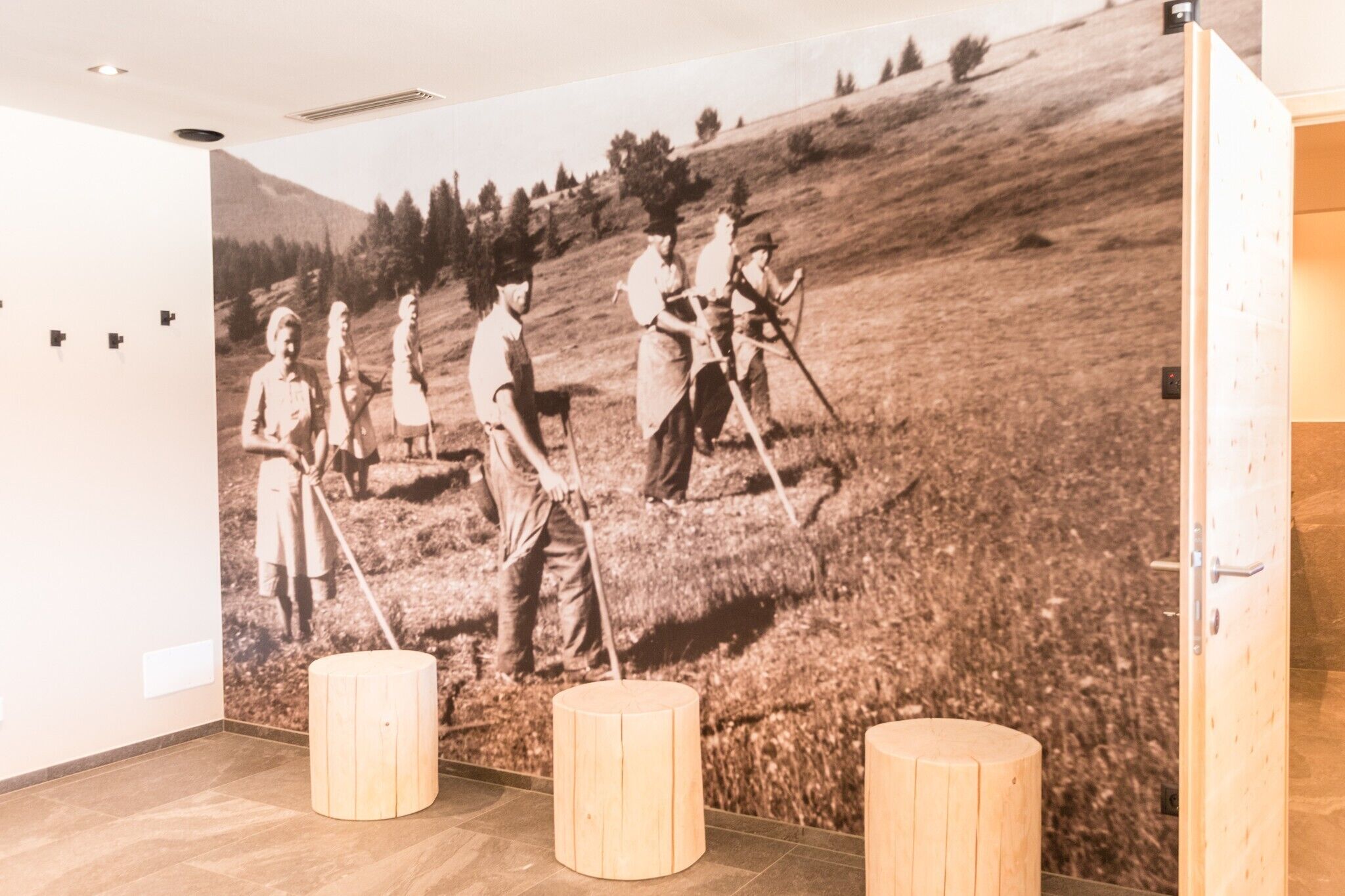 A room with a large black and white photo of people in a field, wooden stools, and a marble floor.