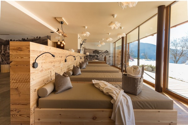 A room with wooden walls, multiple beds, a large window with a mountain view, and a hanging light fixture.