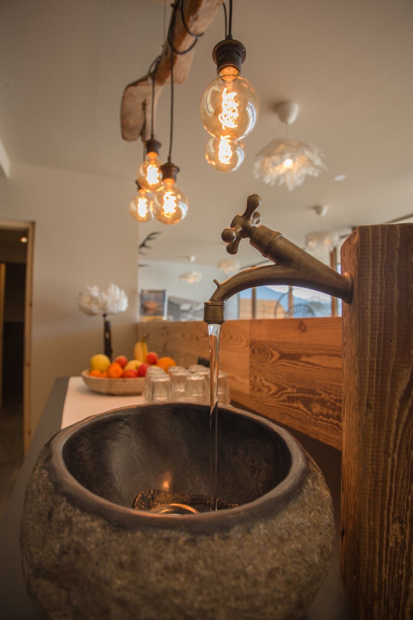Een stenen wasbak met water dat uit een houten kraan stroomt, omringd door hangende lampen.