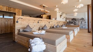 Una spa con pareti in legno, diversi lettini da massaggio e un affresco raffigurante un paesaggio rurale.