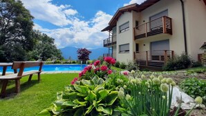 Un edificio a due piani con piscina, immerso nel verde e fiorito.