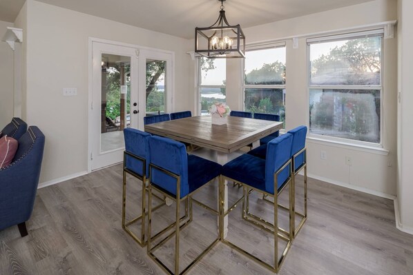 A dining area with a wooden table and blue upholstered chairs, a chandelier, and large windows with a view.