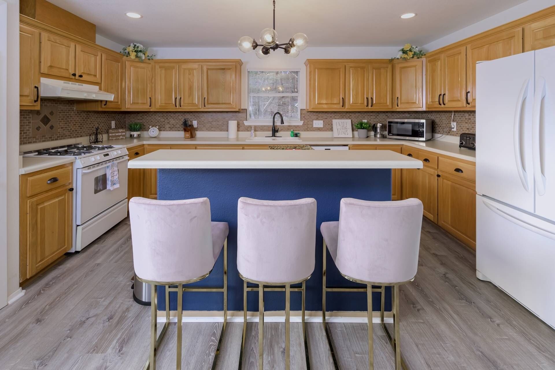 A modern kitchen with wooden cabinets, a central island with bar stools, a stainless steel refrigerator, and a microwave.