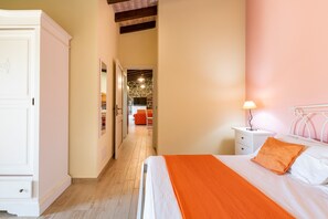 A bedroom with a bed, a nightstand, a wardrobe, and a hallway leading to a kitchen area.