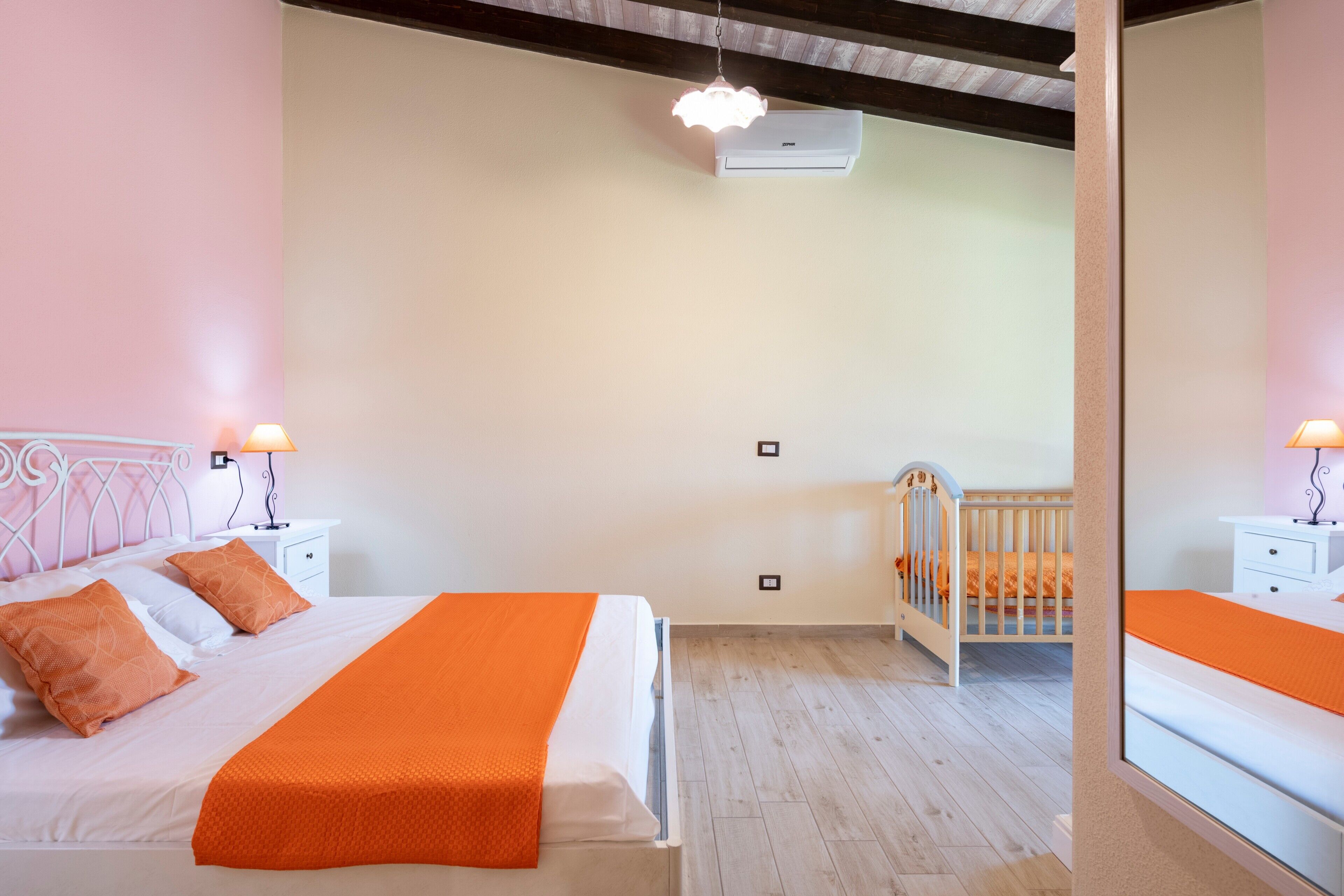 Un dormitorio con cama, mesitas de noche, cuna y espejo.
