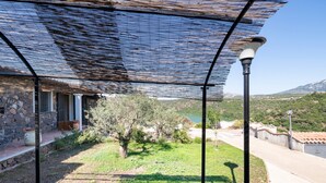 A covered outdoor area with a stone building, a tree, and a view of a lake and hills. - Apartment Casa Sole with Mountain View, Wi-Fi, Garden & Terrace (Dorgali)
