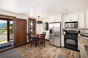 Una cocina moderna con armarios blancos, electrodomésticos de acero inoxidable y un comedor con sillas de madera y una mesa redonda.