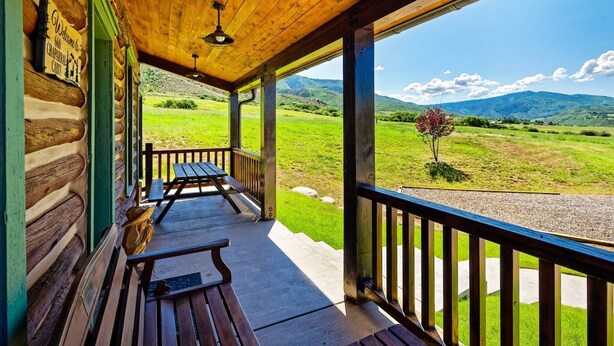 A wooden porch with a bench and a table, overlooking a green landscape with mountains in the distance. - Great Cabin Experience - Stay Near to Aspen, AC (Woody Creek)