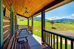 Un porche de madera con un banco y una mesa, con vistas a un paisaje verde con montañas al fondo.