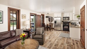 A modern living room with a brown leather sofa, a wooden coffee table with a vase of flowers, and a dining area with wooden chairs and a round table. - Great Cabin Experience - Stay Near to Aspen, AC (Woody Creek)