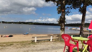 Une vue sur le lac, avec une plage de sable, une rangée de chaises rouges et jaunes, et un petit quai où sont amarrés des bateaux.