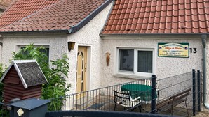 Ein Haus mit rotem Ziegeldach, einem kleinen Garten und einem Schild, das es als Ferienwohnung kennzeichnet.
