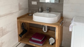 Ein modernes Badezimmer mit einem Holzbadschränkchen, einem weißen Waschbecken und einem großen Spiegel.
