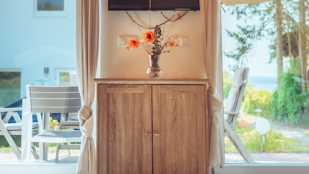 Une pièce avec un meuble en bois, un téléviseur à écran plat fixé au mur et une fenêtre avec des rideaux.
