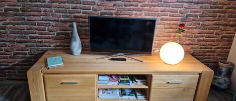 Un meuble de rangement en bois abritant un téléviseur à écran plat, un vase, une télécommande et une lampe allumée, le tout placé devant un mur en briques.