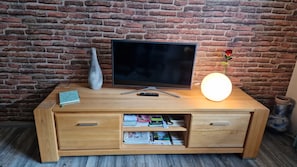 En möbel i trä, avsedd för underhållning, med en platt-TV, en vas, en fjärrkontroll och en tänd lampa, placerad framför en tegelvägg.