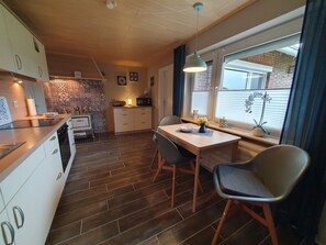 Una cocina con encimera de madera, una mesa de comedor con sillas, un ventanal con persianas y un salpicadero decorado.