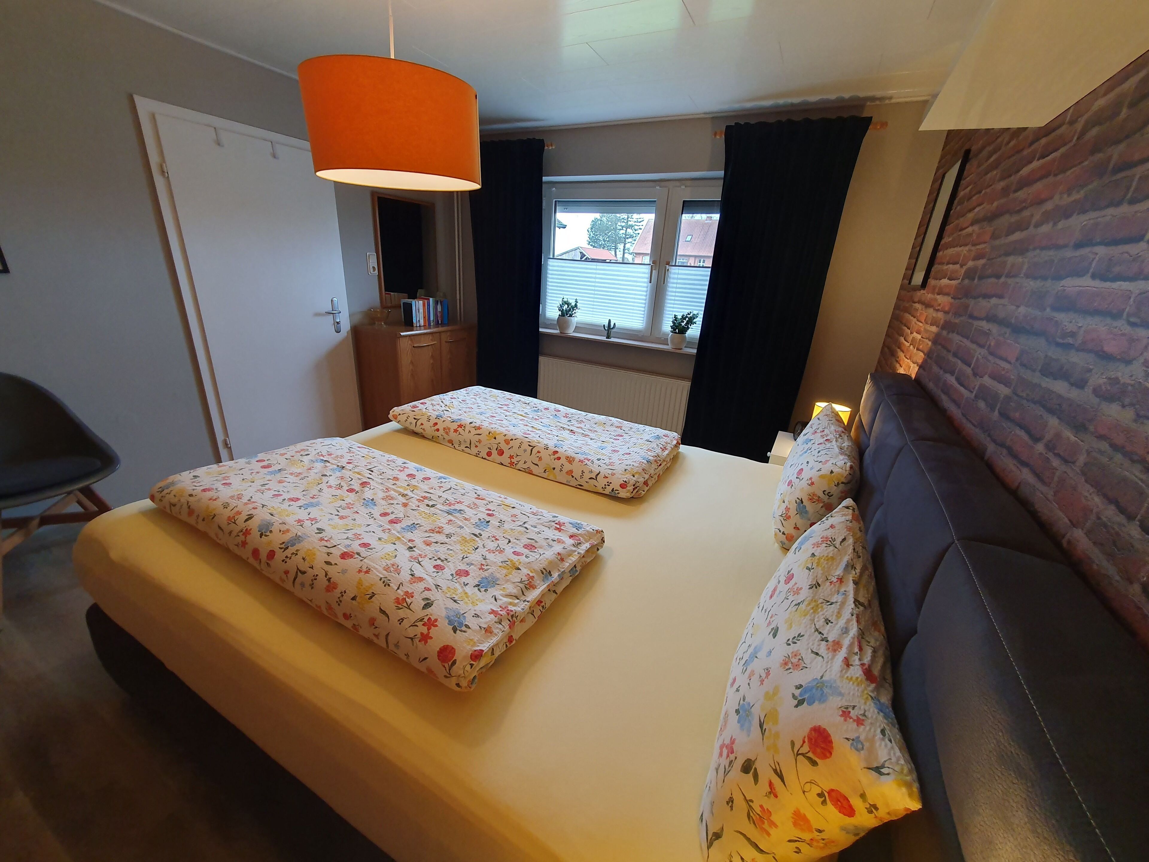 Un dormitorio con dos camas, un sofá, una silla, una ventana con cortinas, una pared de ladrillo y una lámpara colgante.