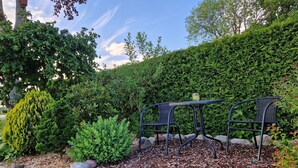 A garden with a table and chairs, surrounded by various plants and a hedge. - Ferienwohnung Kanalblick 35520 - Ferienwohnung Kanalblick (Uplengen)