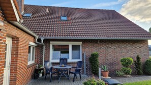 A brick house with a tiled roof, a patio with a table and chairs, and potted plants.