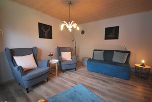 Ein Wohnzimmer mit einem blauen Sofa, zwei Sesseln, einem kleinen Tisch mit einer Vase, einem blauen Teppich und einer Chandelüster.