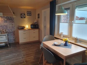 A kitchen with a microwave, a small table with chairs, a window with blinds, and a decorative vase with flowers.