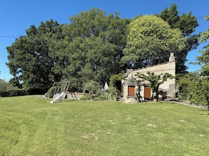 A stone house with a wooden door, a swing set, and a grassy yard.