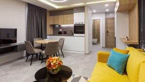 Una sala de estar moderna con un sofá amarillo, una mesa de comedor con sillas y una cocina con un televisor y un florero.