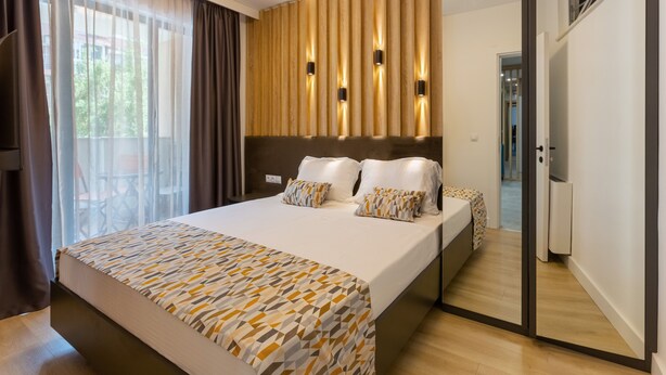 Habitación de hotel moderna con una cama grande, cabecera de madera y vistas al exterior a través de cortinas traslúcidas.