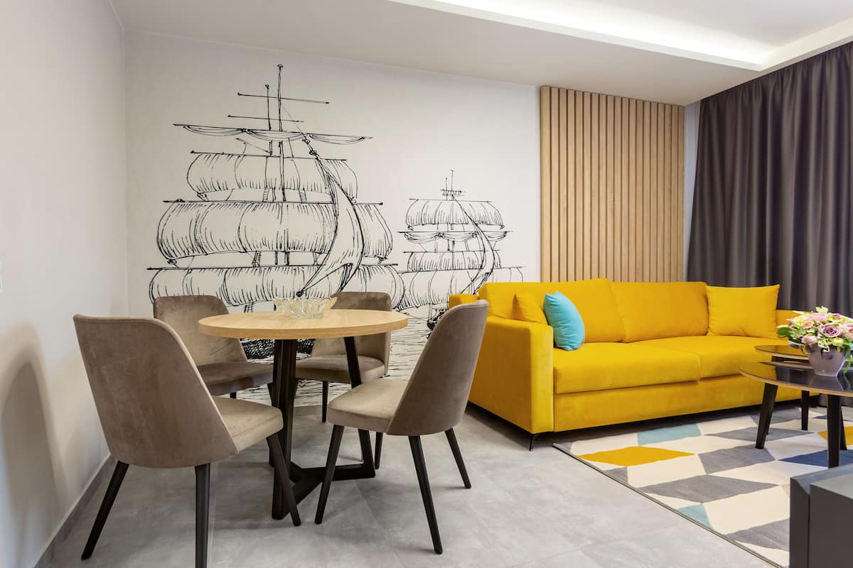 A modern living room with a yellow sofa, a dining table with chairs, and a wall mural of a ship.